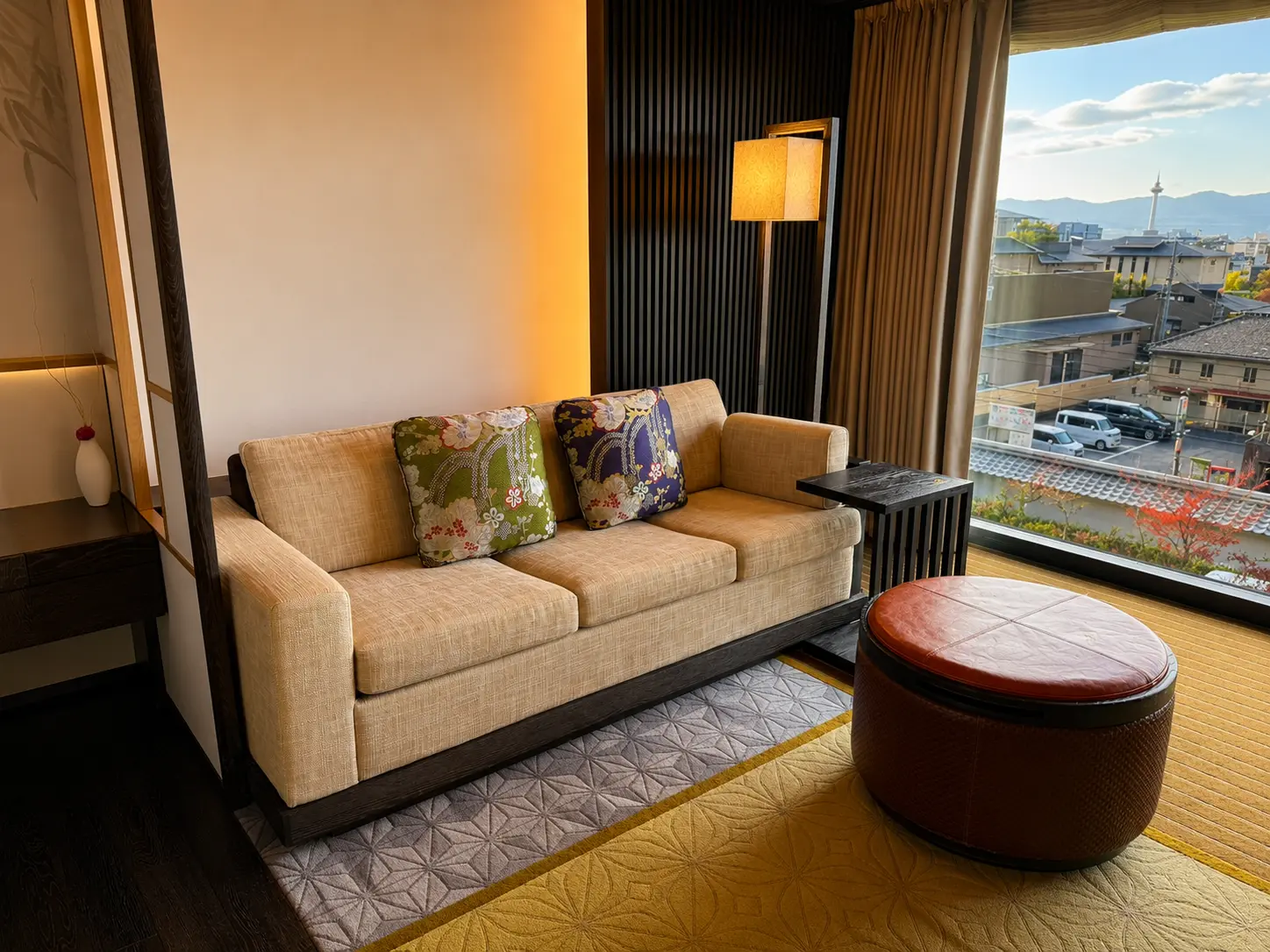 Sitting area in a Deluxe Room at Four Seasons Hotel Kyoto with sofa, Japanese-style cushions and views across Kyoto toward Kyoto Tower.