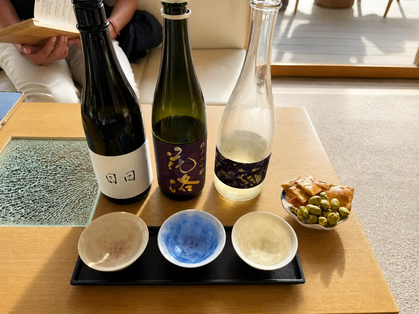 Japanese sake tasting at FUJU Tea House at Four Seasons Hotel Kyoto with three sake bottles and small snacks.