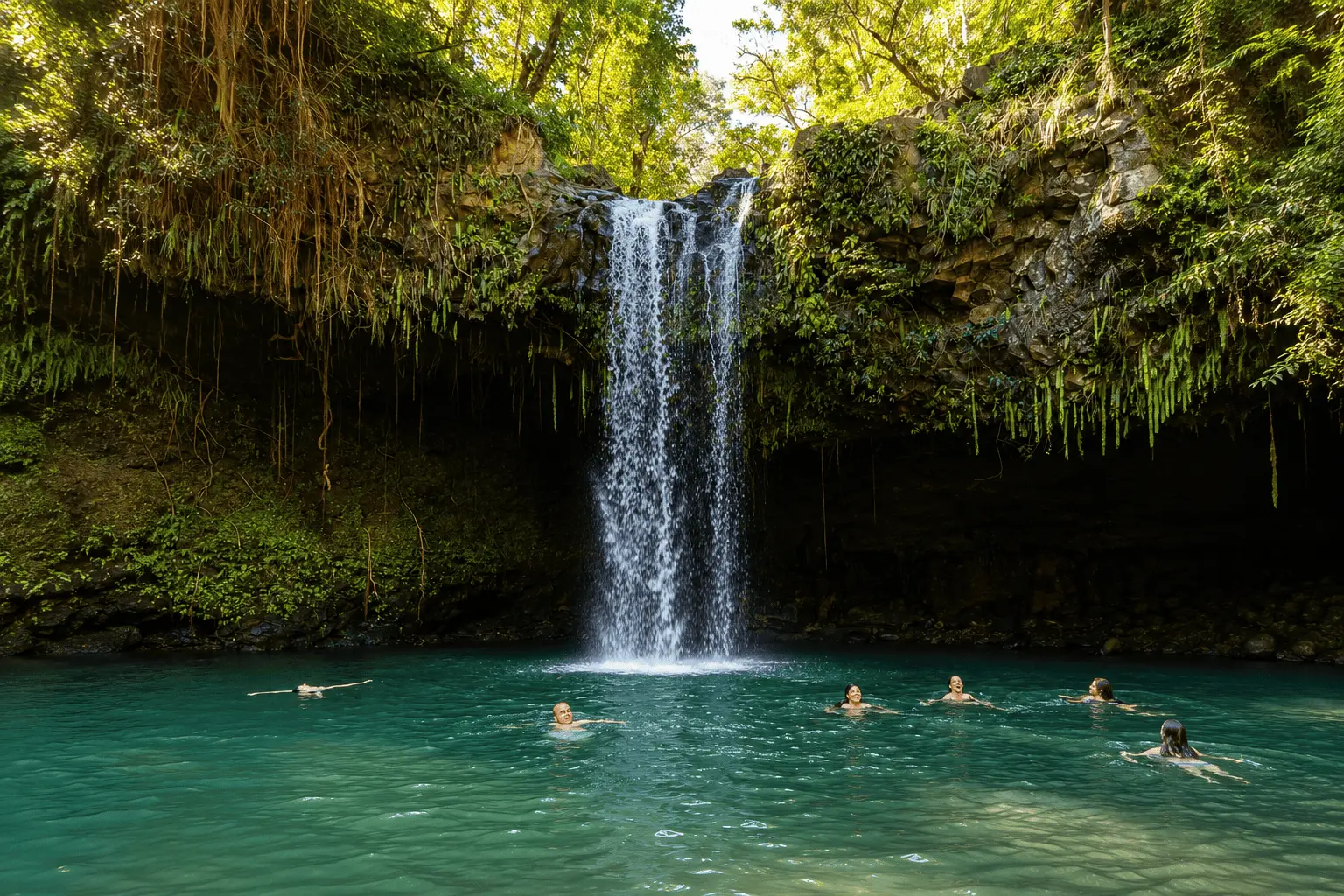 Travelers swimming beneath a waterfall along the Road to Hana in Maui, Hawaii.