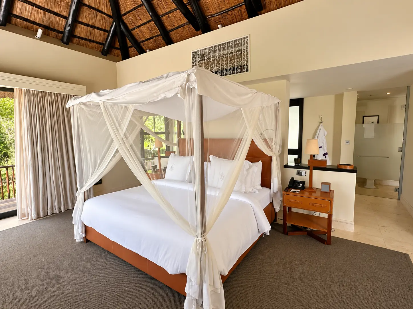 King canopy bed with mosquito netting and thatched ceiling in a One-Bedroom Villa at Four Seasons Safari Lodge Serengeti, Tanzania.