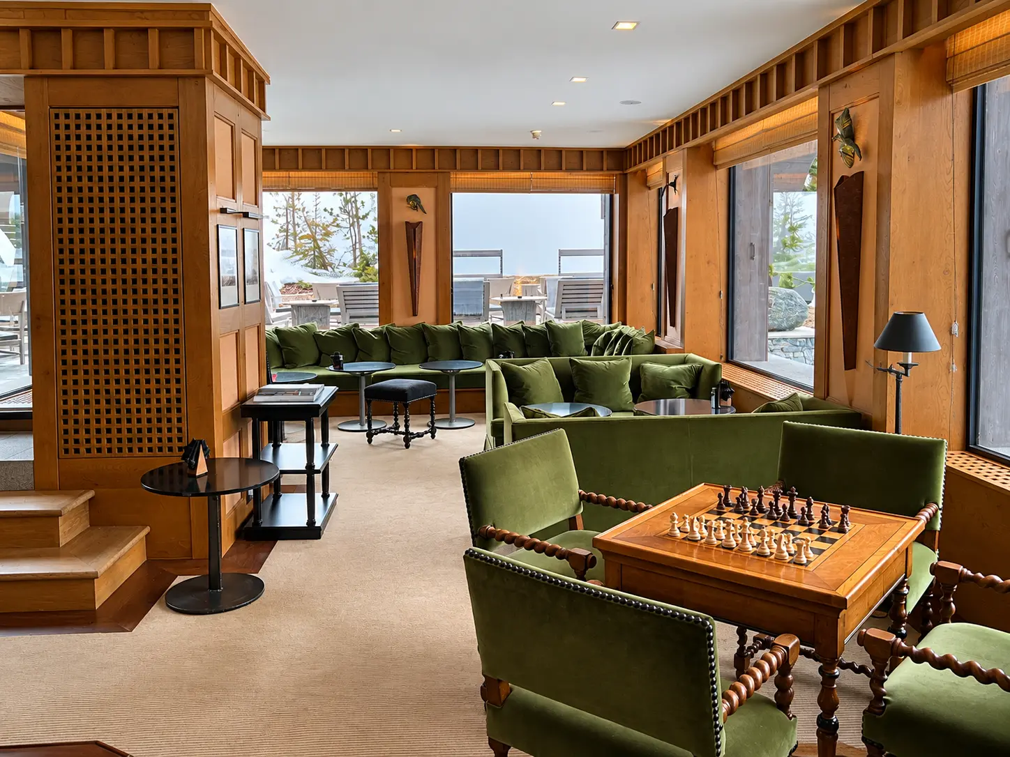 Lounge at Aman Le Mélézin with green seating, timber interiors and a chess table overlooking the snow.