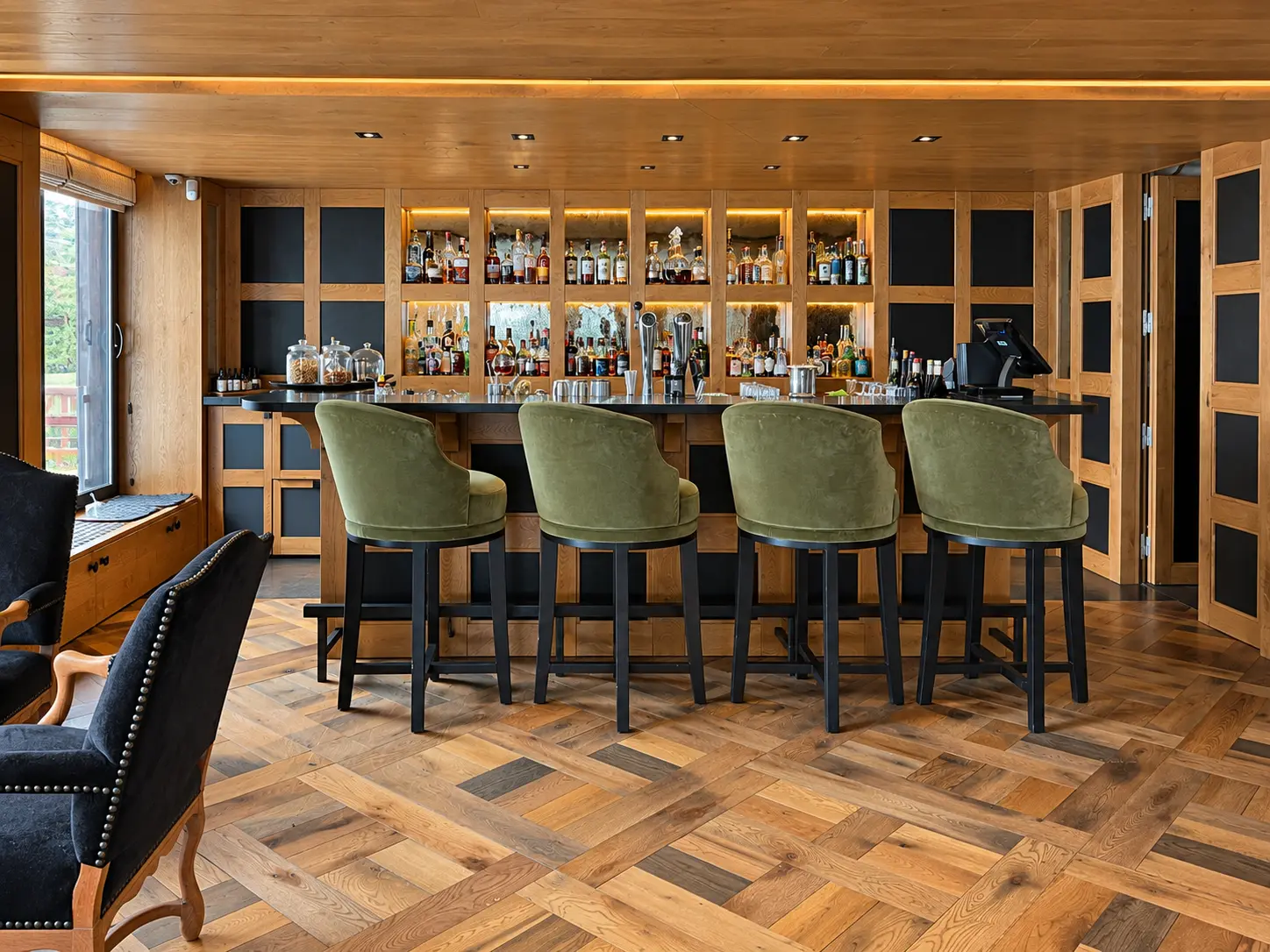 Bar at Aman Le Mélézin in Courchevel 1850 with warm timber cabinetry and green bar stools.