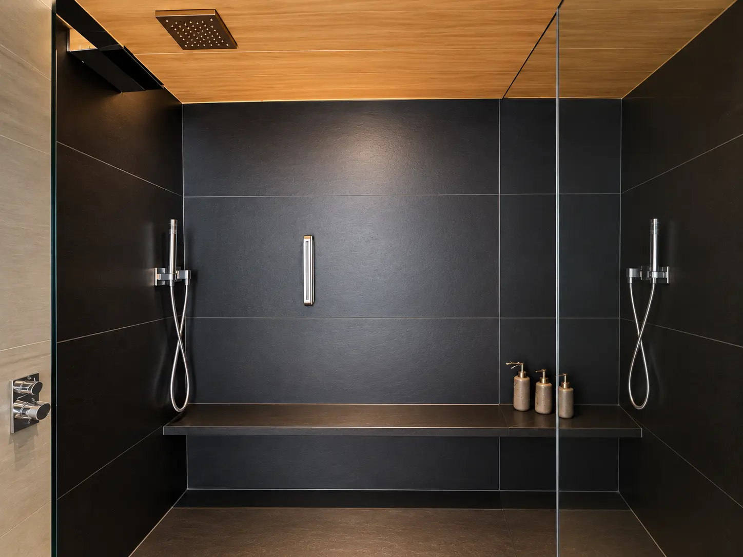 Large walk-in rainfall shower with dark stone walls and built-in bench at Aman Le Mélézin.