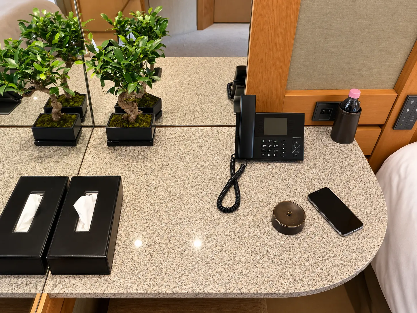 Stone-topped bedside area in a Chambre Ski Piste at Aman Le Mélézin with telephone, bottled water and small plant.