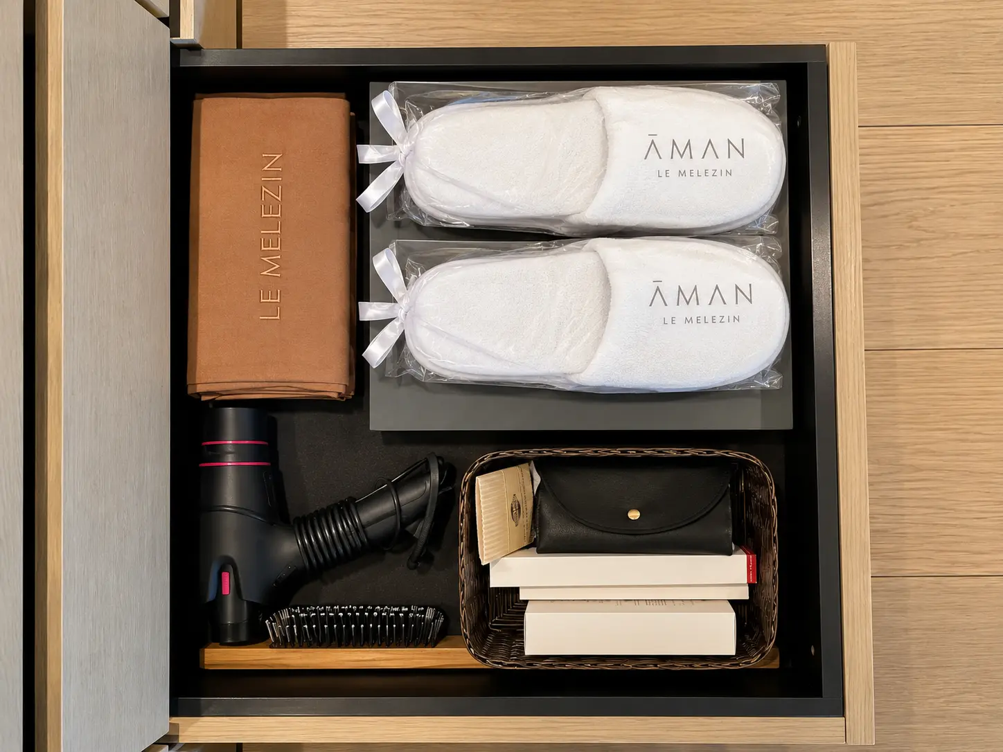 Aman Le Mélézin slippers, hairdryer, brush and guest amenities arranged inside a fitted room drawer.