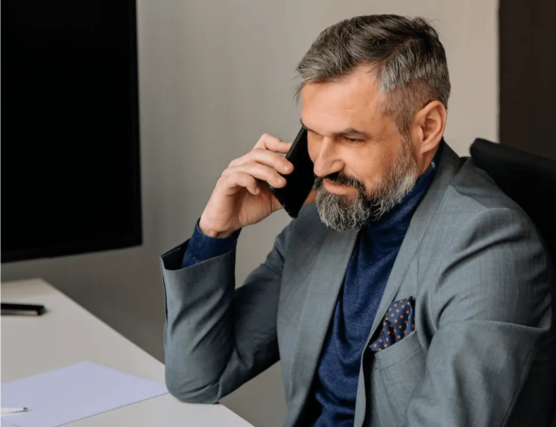 A man sitting at a desk talking on a cell phone.