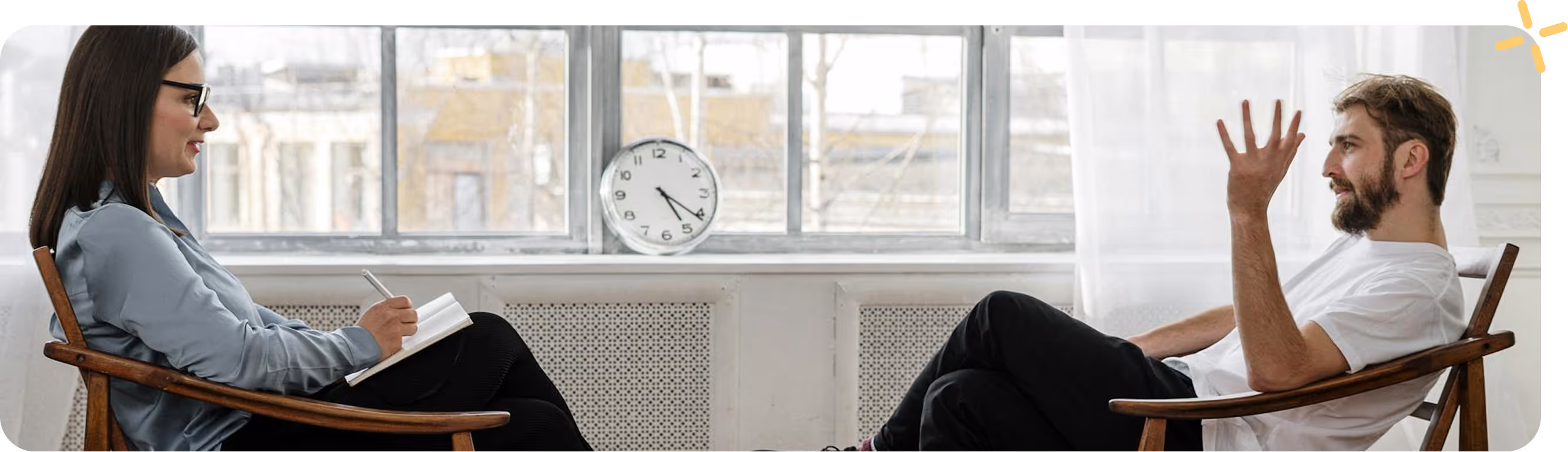 A man and a woman sitting in chairs with a clock in the background.