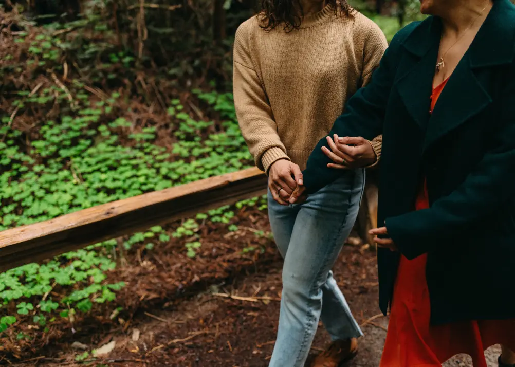 Two women walking arm in arm along a forest path