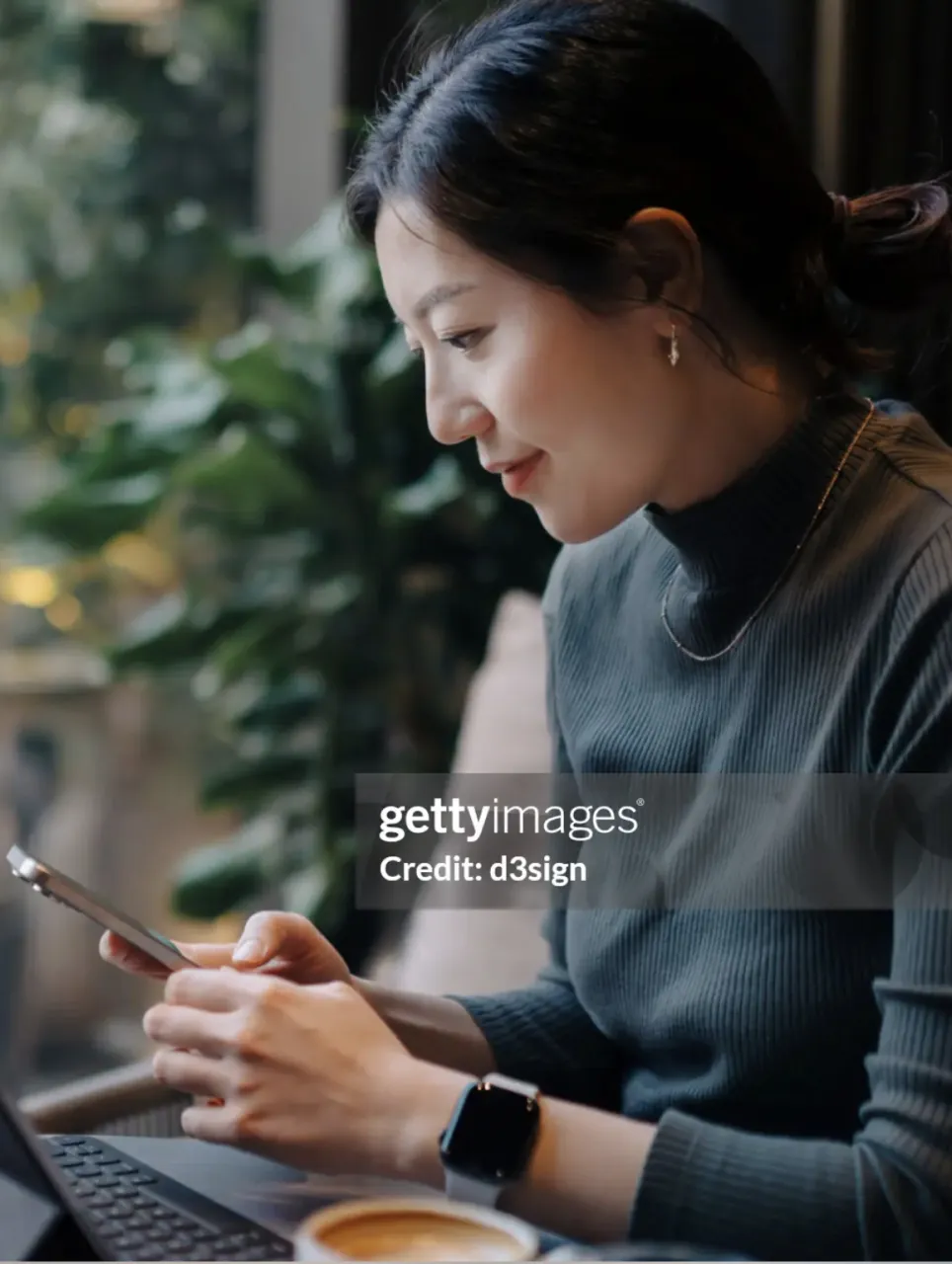 Woman smiling at her phone while using a laptop in a café