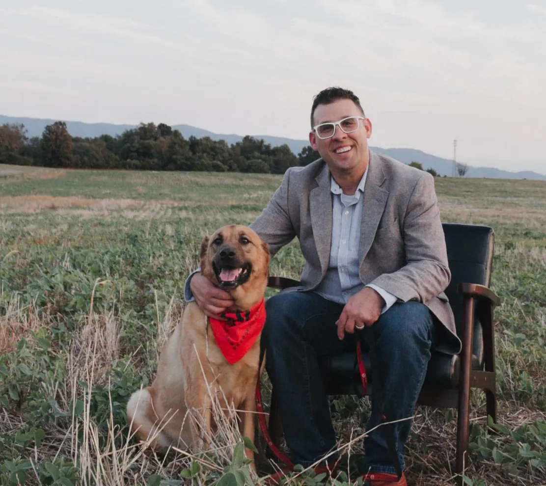 Therapist Tommy Delbridge sitting in a field with his dog