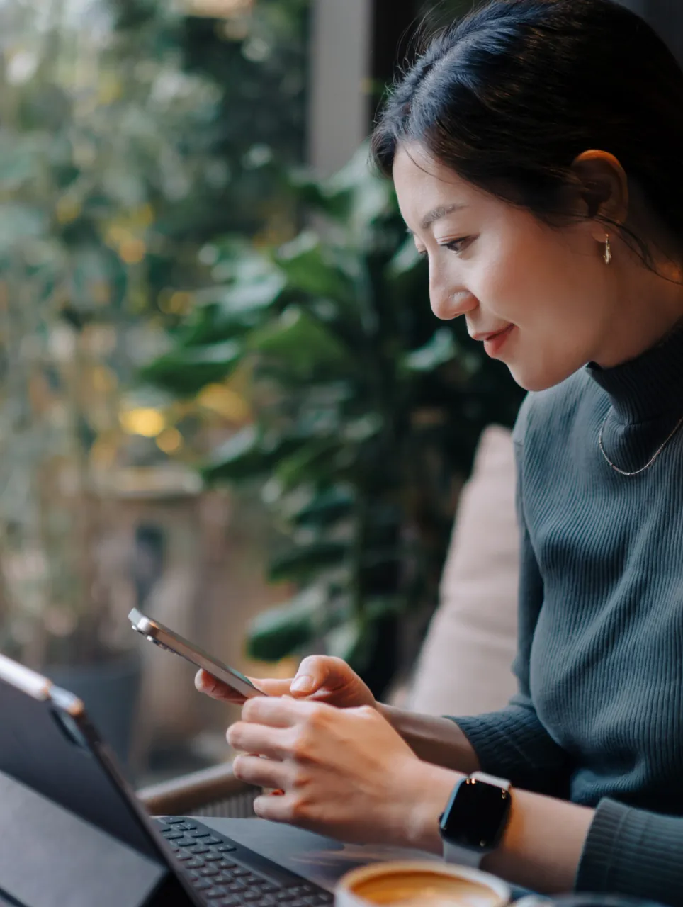 Woman smiling at her phone while using a laptop in a café