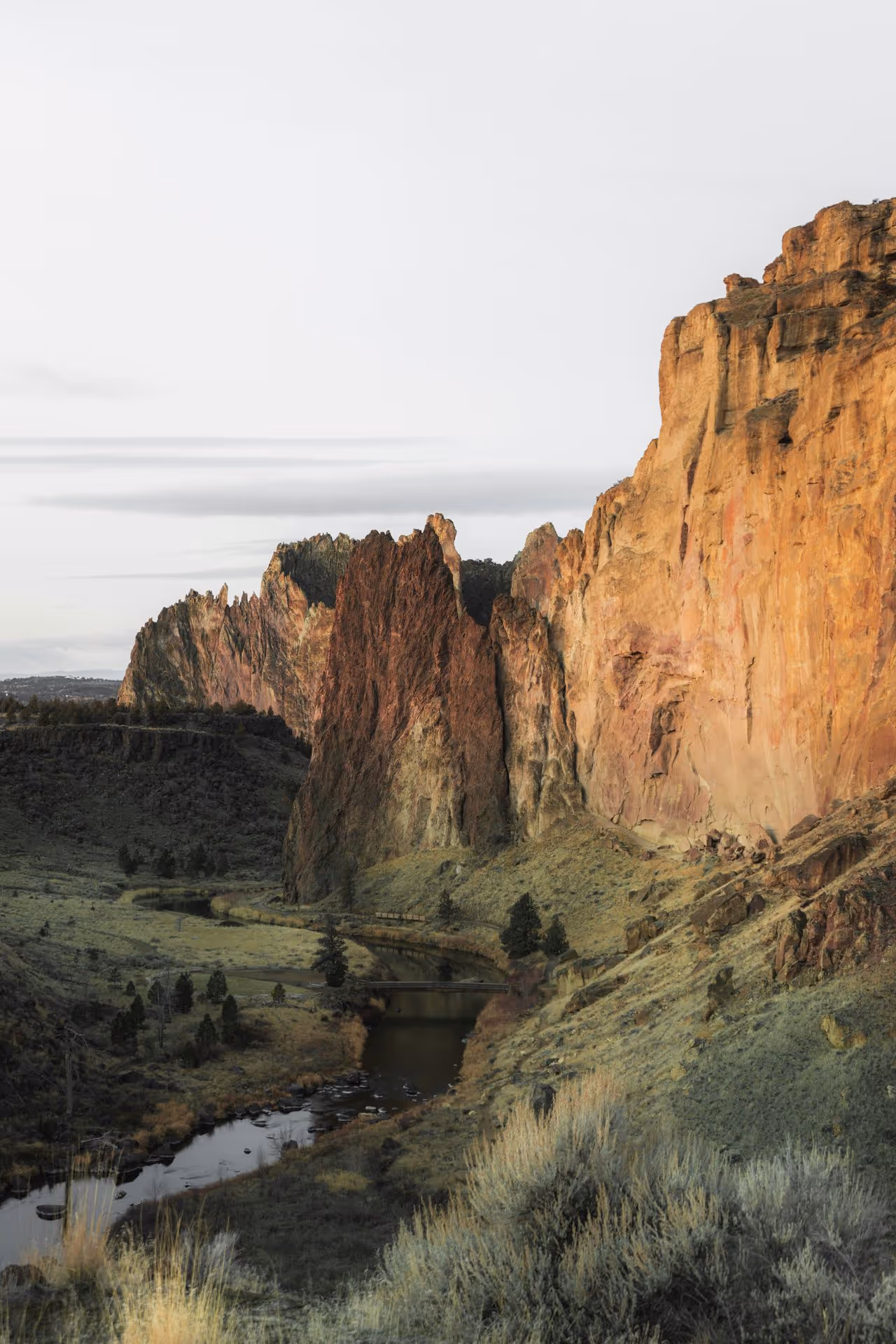 River winding through rocky cliffs with green vegetation under a clear sky at sunset.