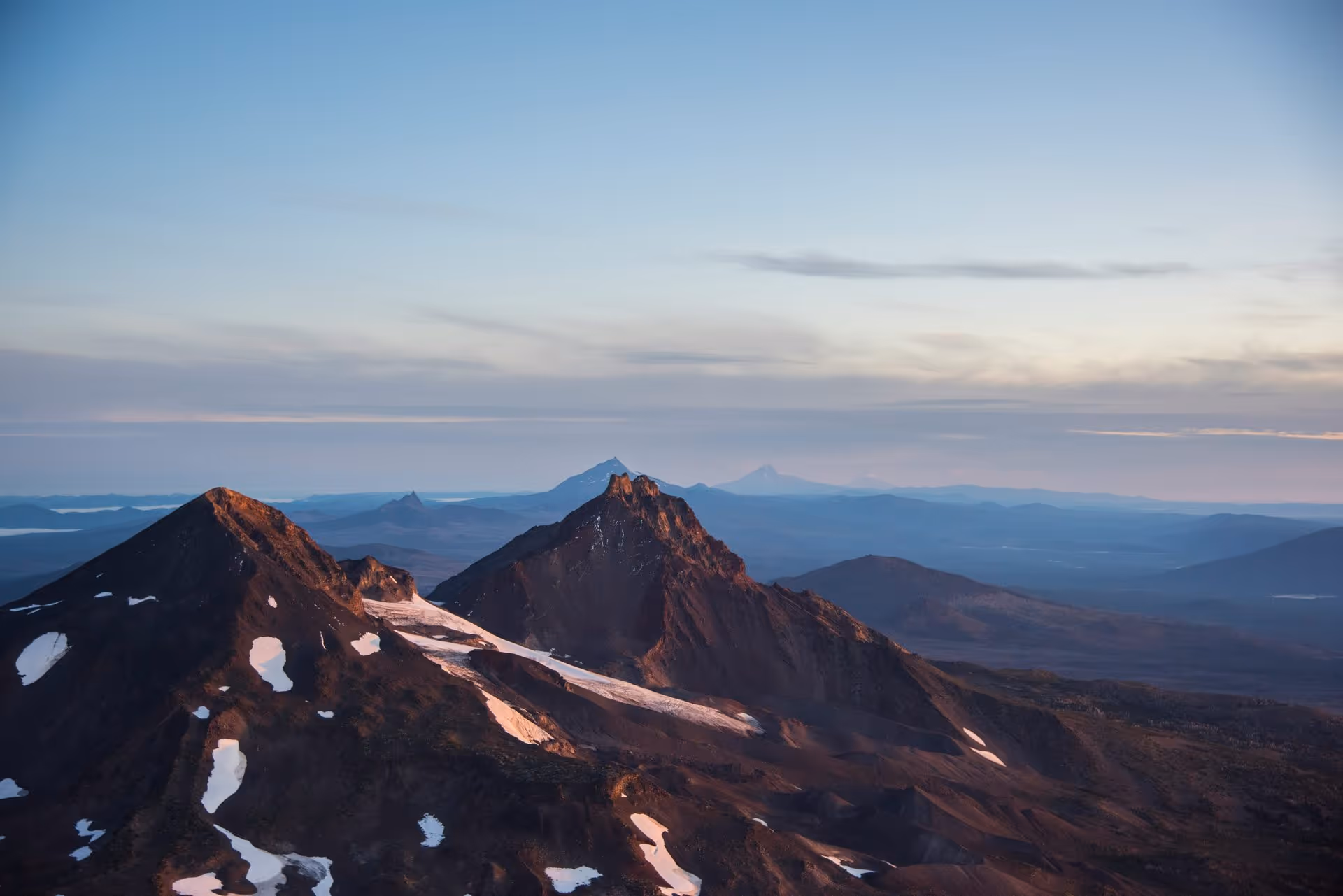 Mountain peaks with patches of snow under a clear blue sky at sunrise or sunset.