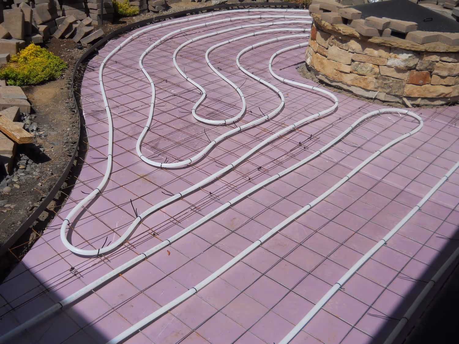 White tubing arranged in curves on a purple grid base for radiant floor heating installation.