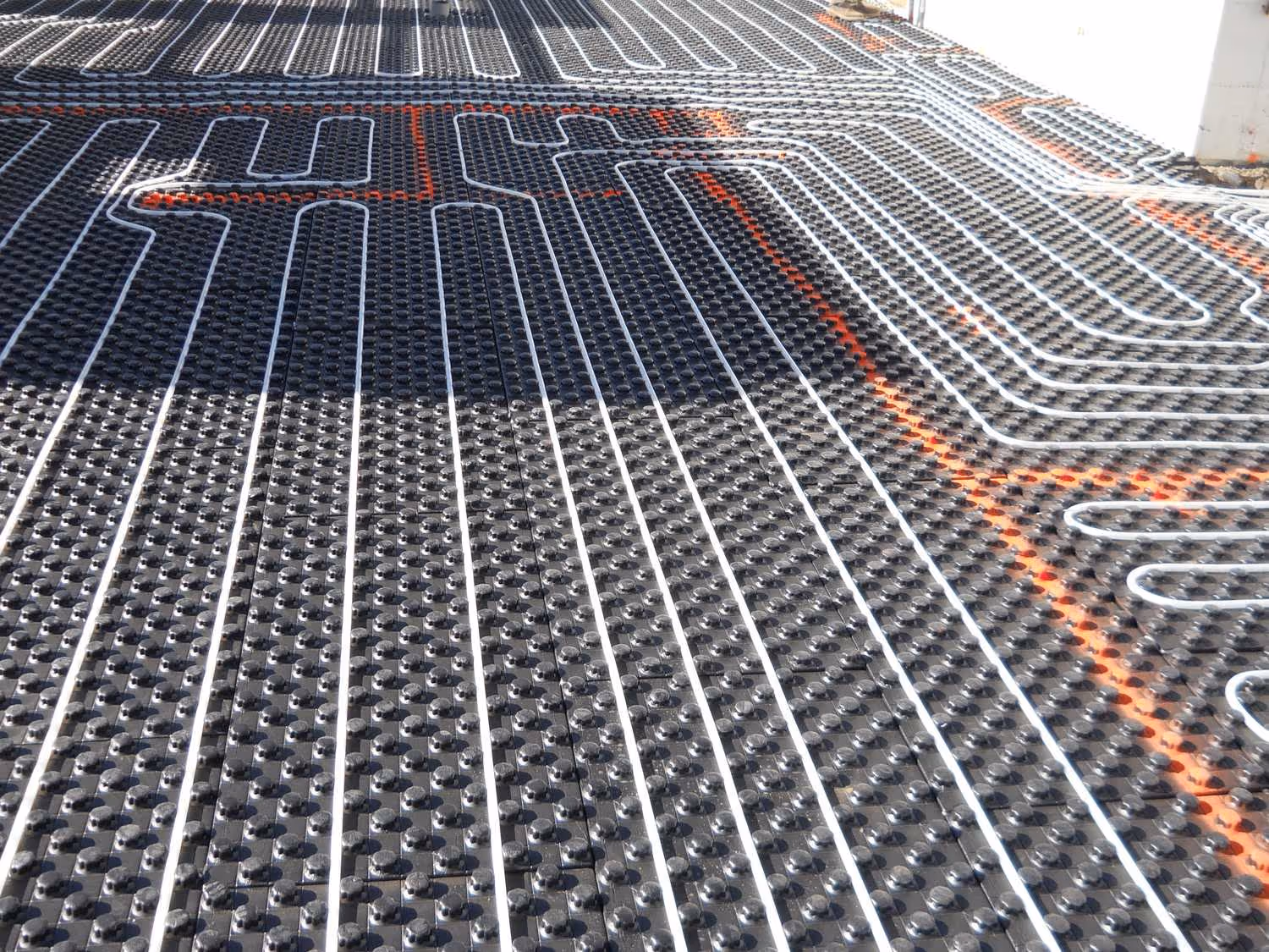 Plastic mat base with white pipes for underslab radiant floor heating installation.