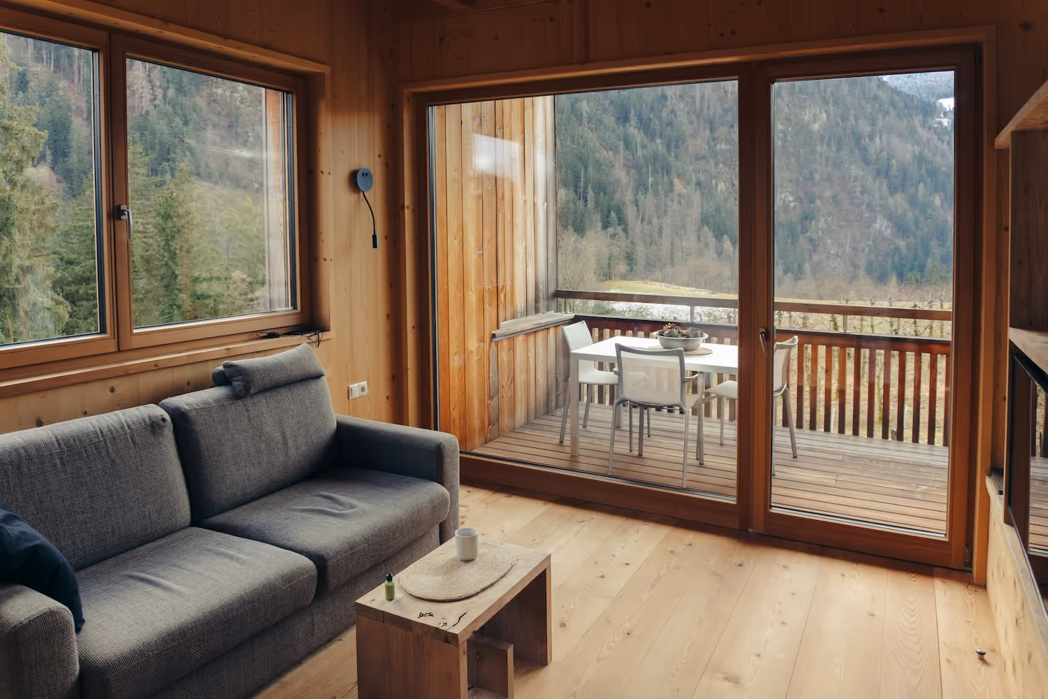 Cozy living room with gray sofa, wooden coffee table, large windows, and mountain view balcony.