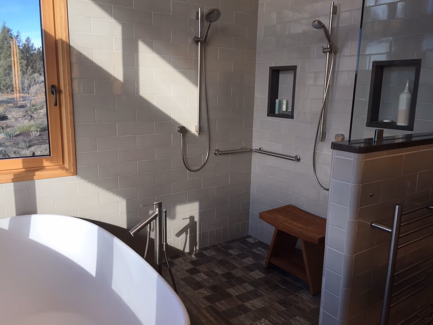 Modern bathroom with a white freestanding tub, wooden window, dual showerheads, and a wooden bench.