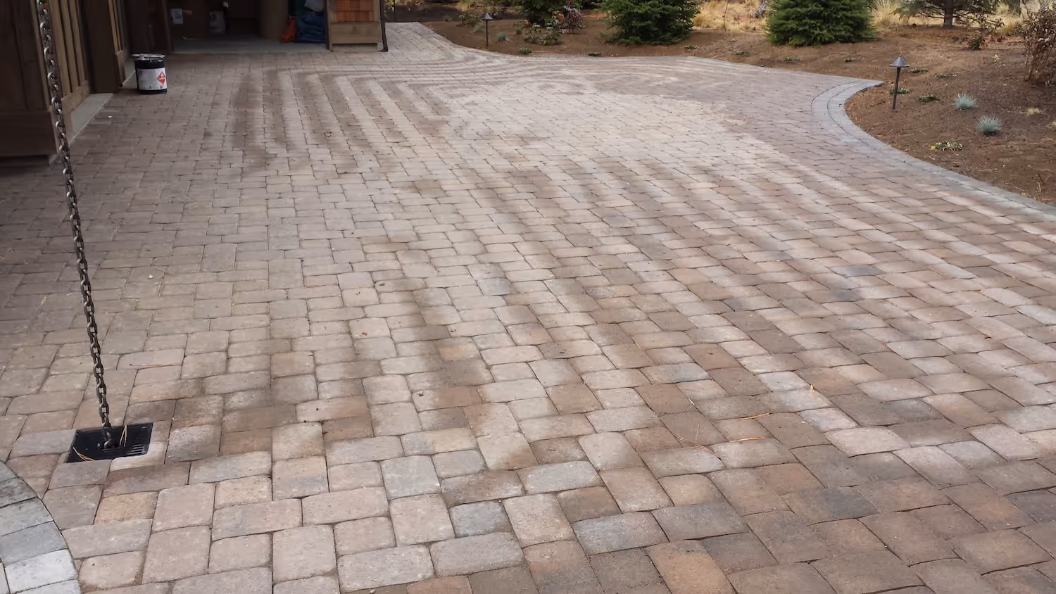Large paved driveway with interlocking bricks bordered by soil and small plants.