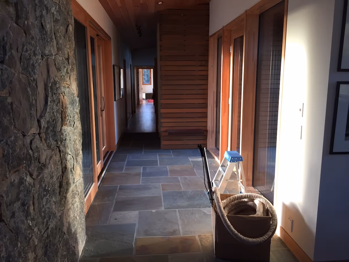Hallway with stone wall, wooden doors, tiled floor, and a box holding a coiled rope and a step ladder.