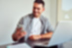 Employee smiling at a smartphone while working at a desk with a laptop