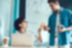 Manager handing a recognition card to an employee at a desk in the office