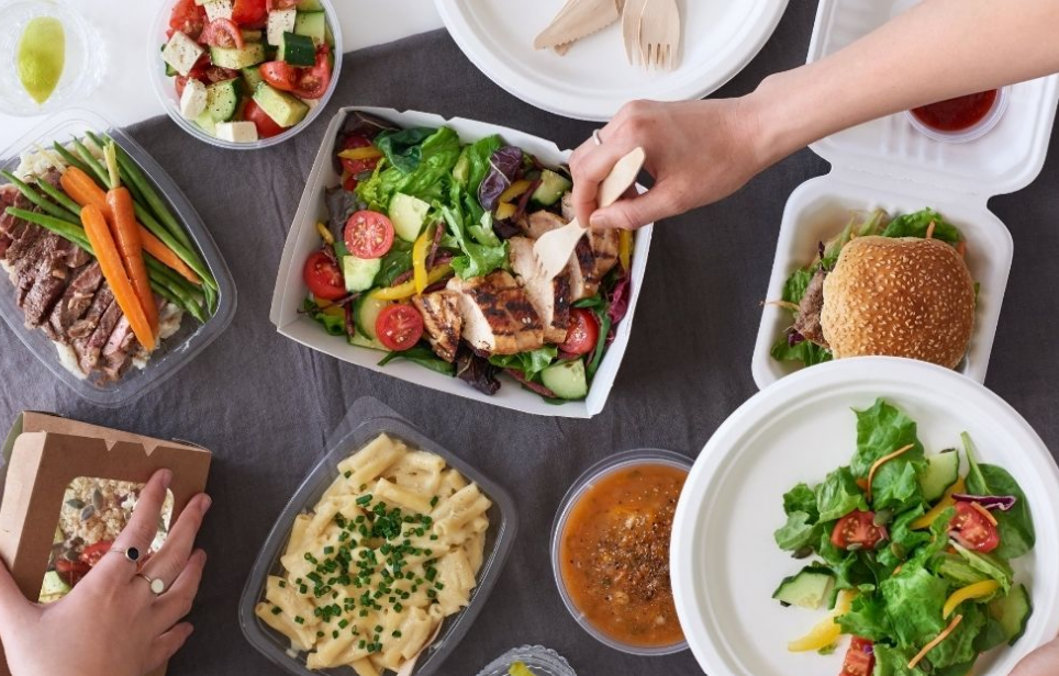 Assorted takeout meal containers with salad, burger, and pasta arranged on a table