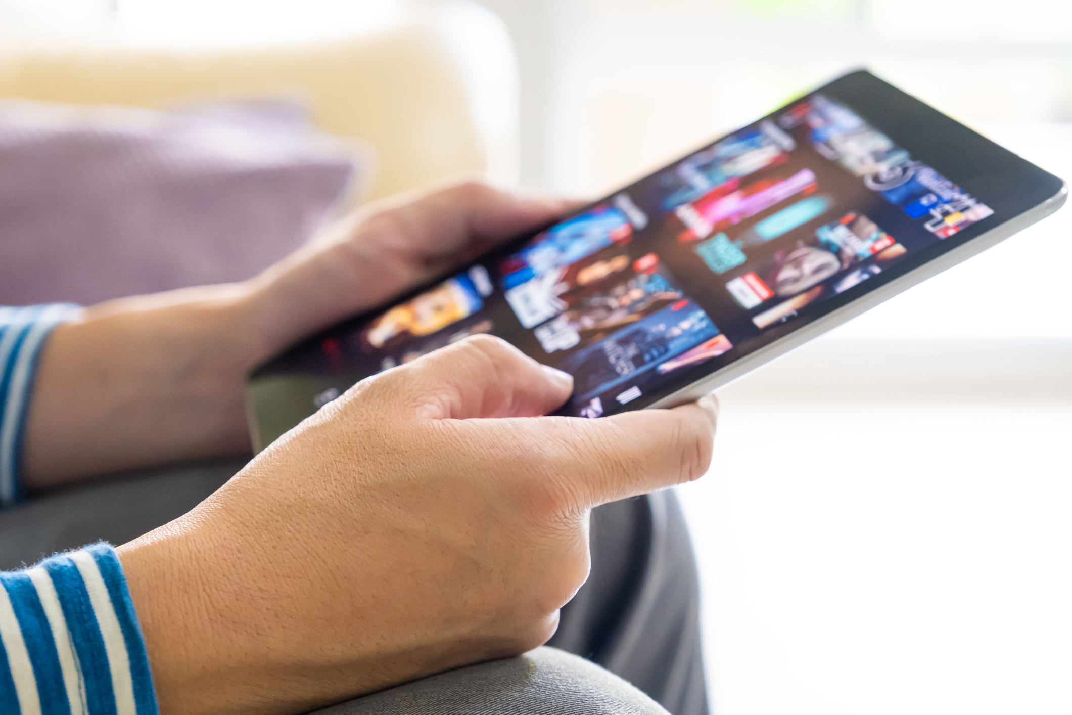 Close-up of hands selecting a movie on a tablet displaying various streaming options.