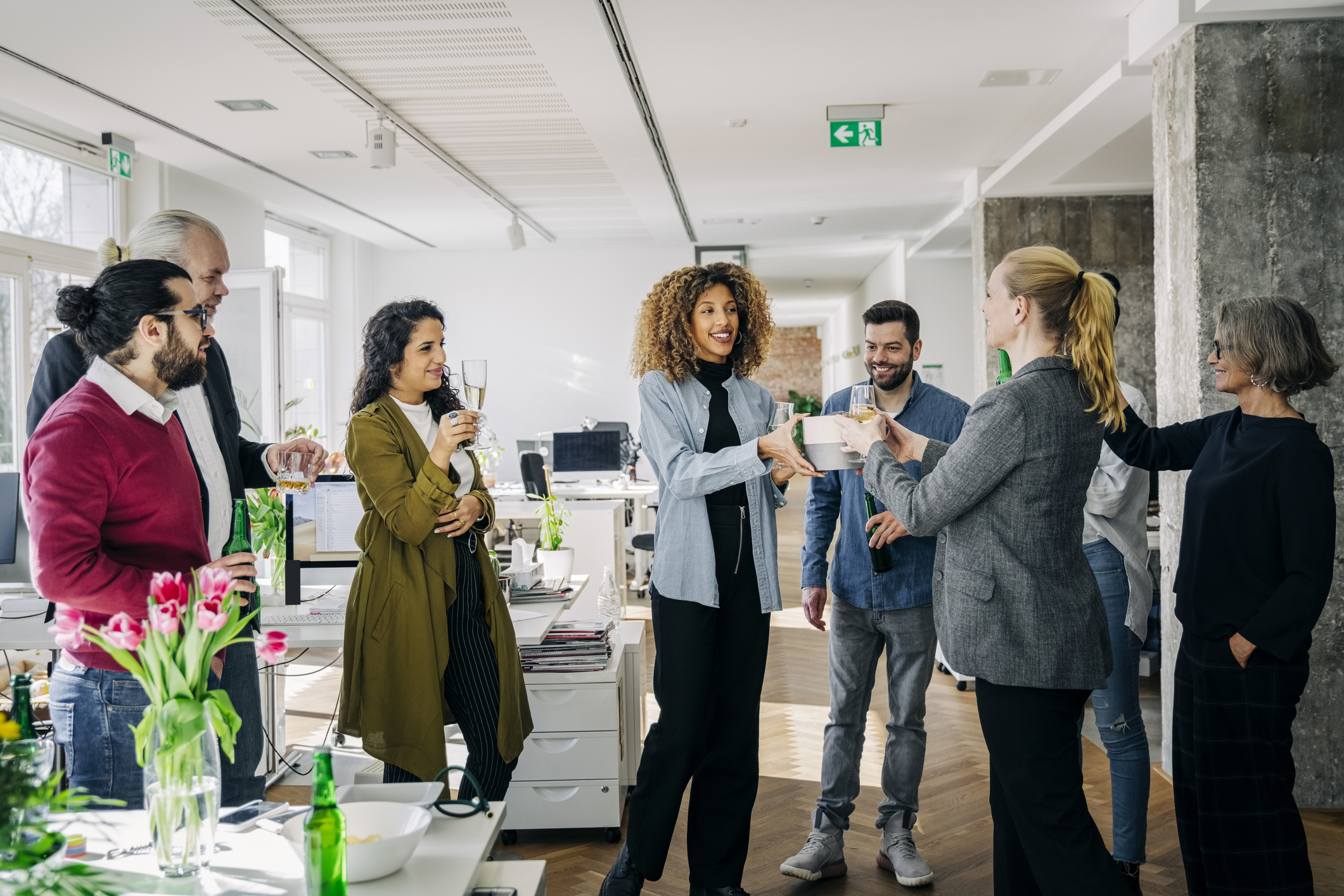 Diverse group of professionals celebrating with drinks in a bright office setting.