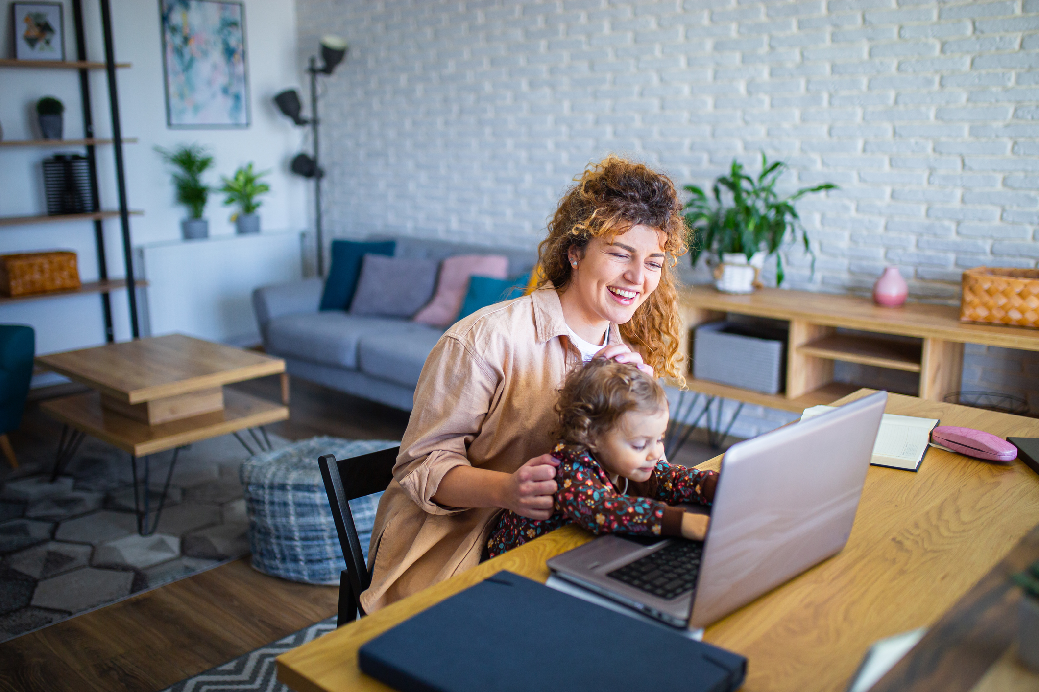Smiling mother working on a laptop with her young child on her lap.