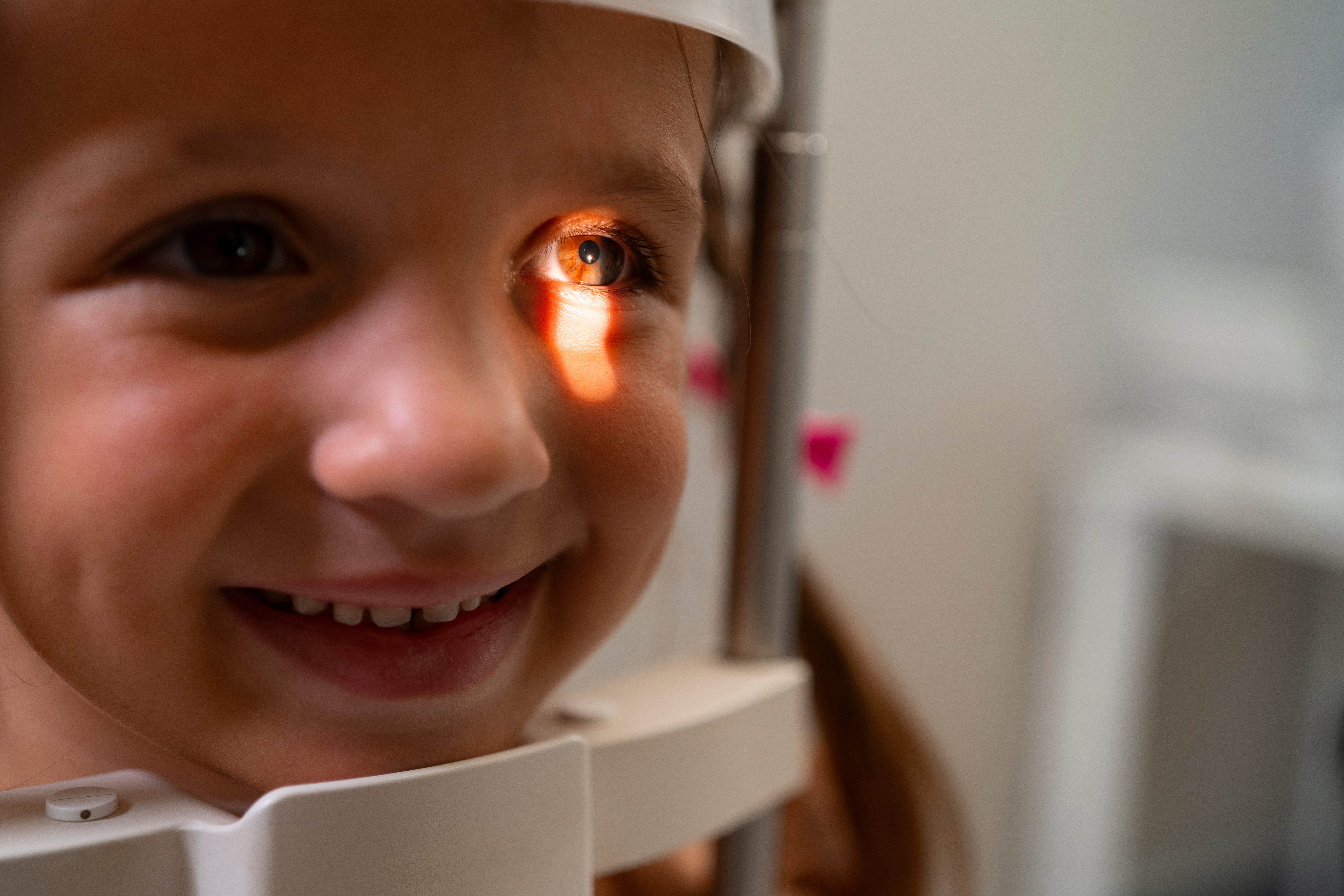 Close-up of a smiling child’s face during an eye exam with light focused on one eye.