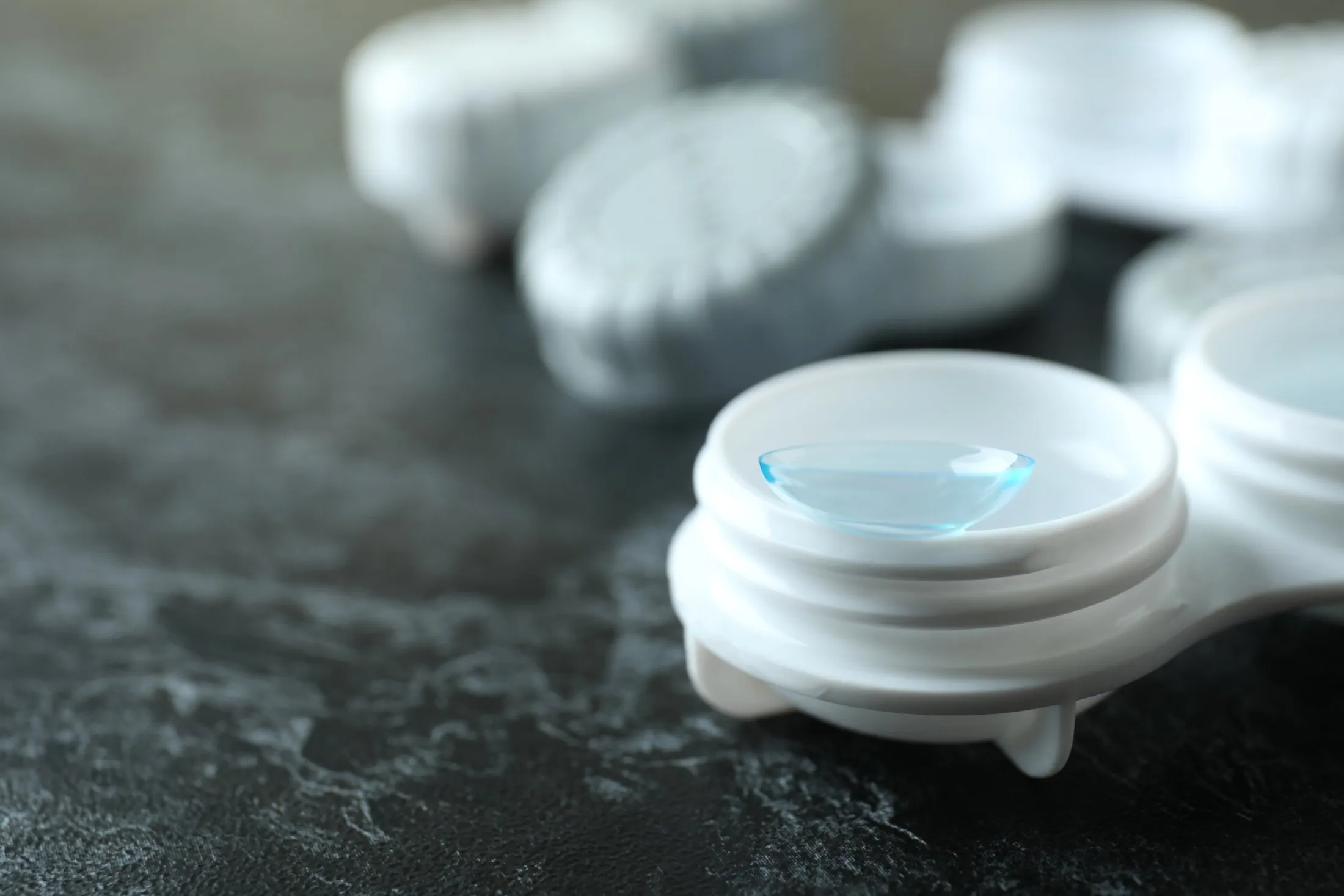 Close-up of a contact lens resting in a white lens case on a dark surface.
