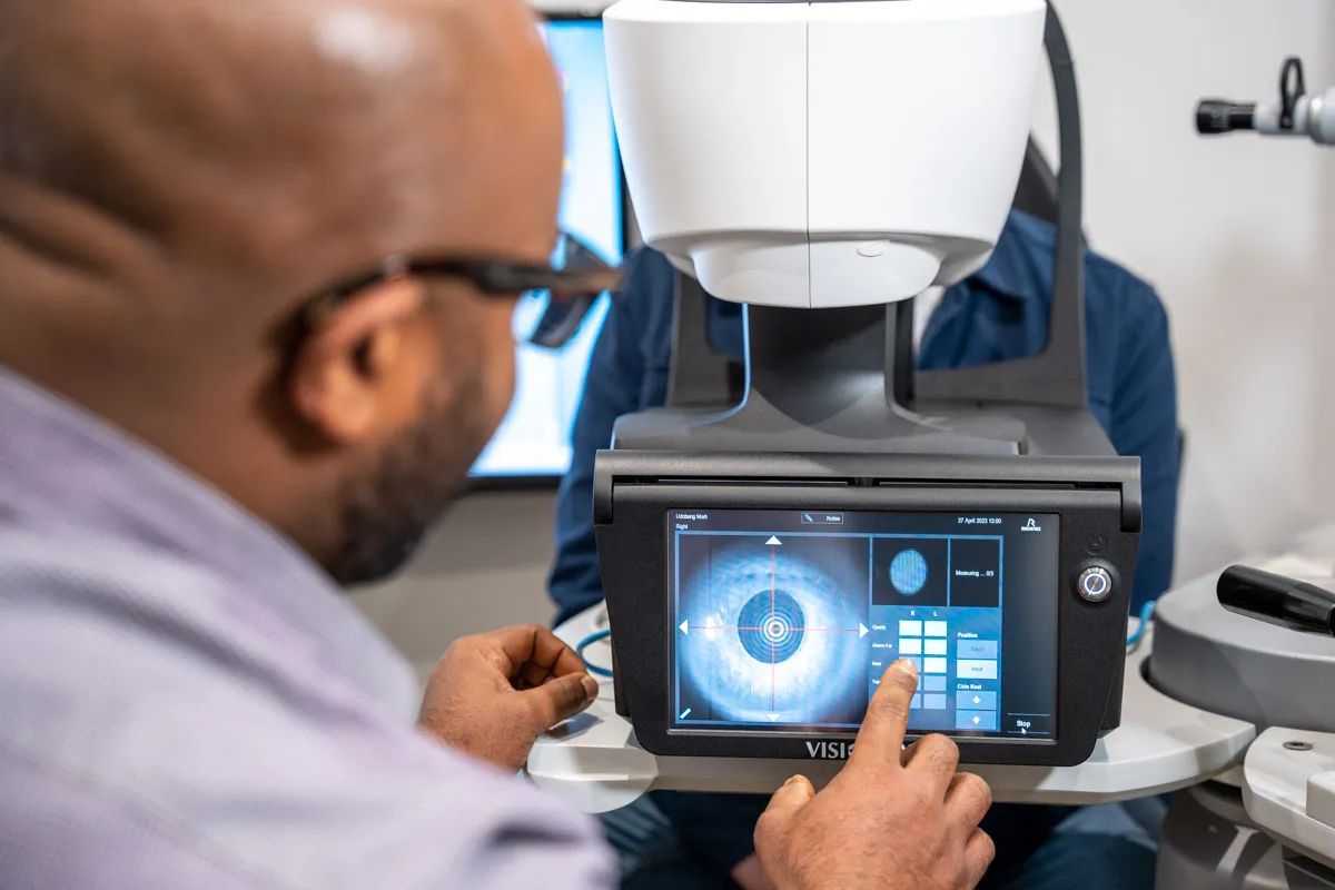 Person interacting with eye examination device displaying a detailed iris scan on the screen.