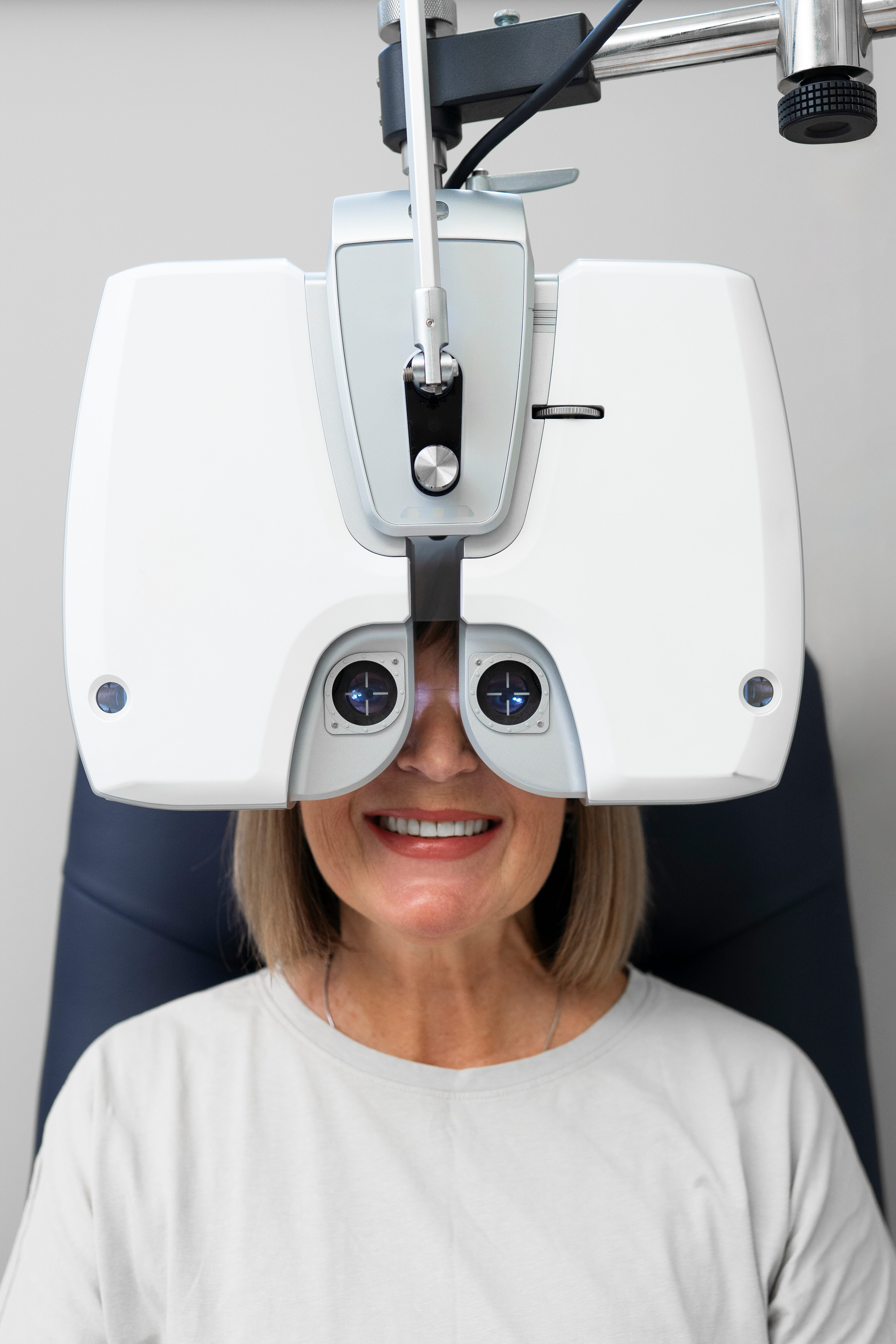 Woman smiling during an eye exam using a phoropter device in an ophthalmologist's office.