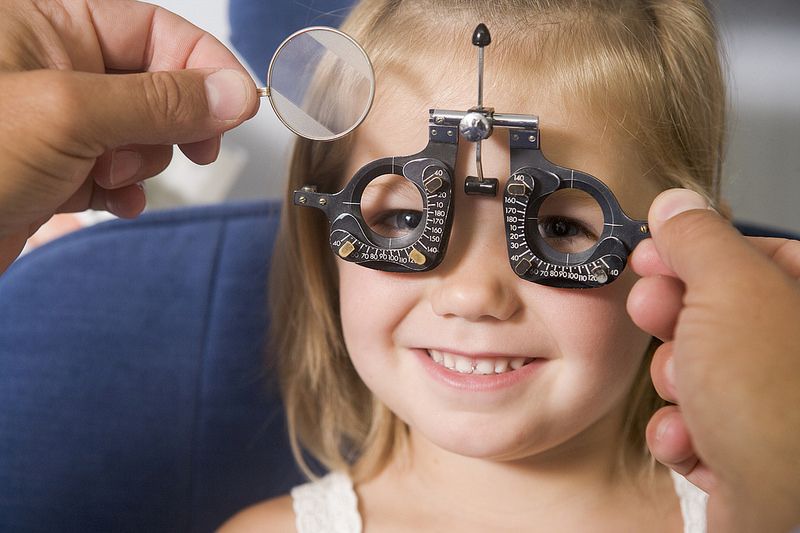 Child smiling as optometrist holds trial frame and lens for eye exam