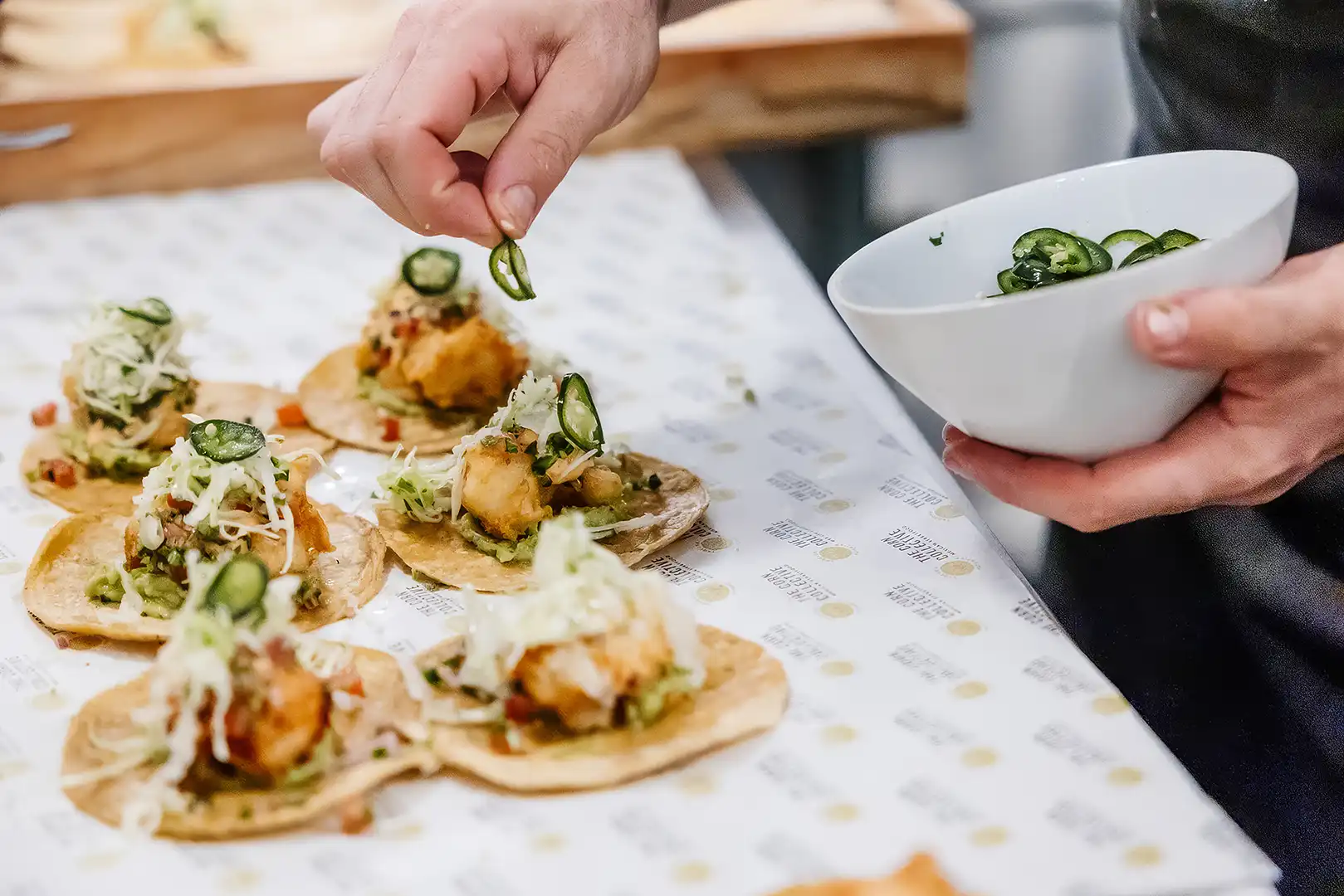 Hand placing sliced jalapeño peppers on fish tacos topped with cabbage on a counter top.