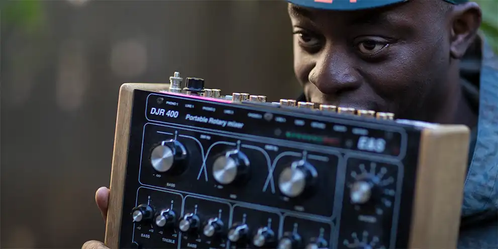 Charlie Dark wearing a green cap with Soweto written on the brim, holding a DJR 400 portable rotary mixer.