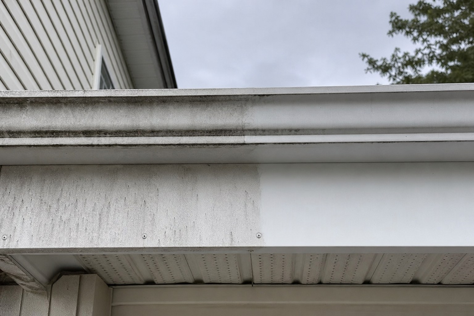 Fascia d'aluminium blanc avec traces de ruissellement noires, moitié de la section déjà nettoyée