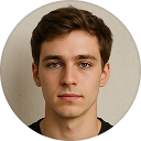 Portrait of a young man with short brown hair and neutral expression against a beige background.