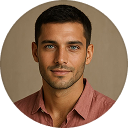 Portrait of a man with short dark hair and blue eyes wearing a red shirt against a brown background.