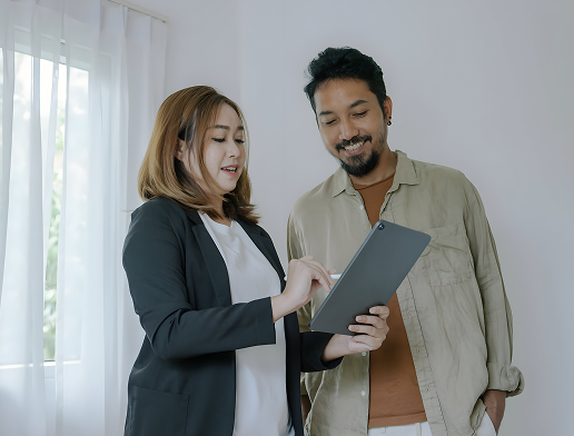 A woman and a man looking at a tablet together in a bright room with a sheer curtain.