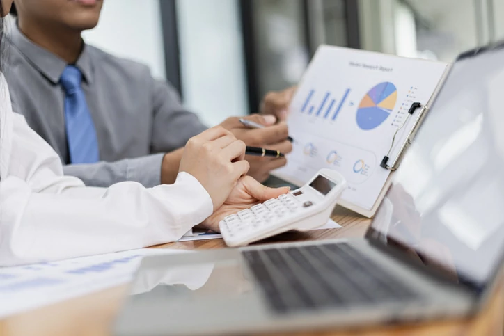Deux personnes consultant des documents avec données graphiques à côté d'une calculatrice et d'un ordinateur portable.