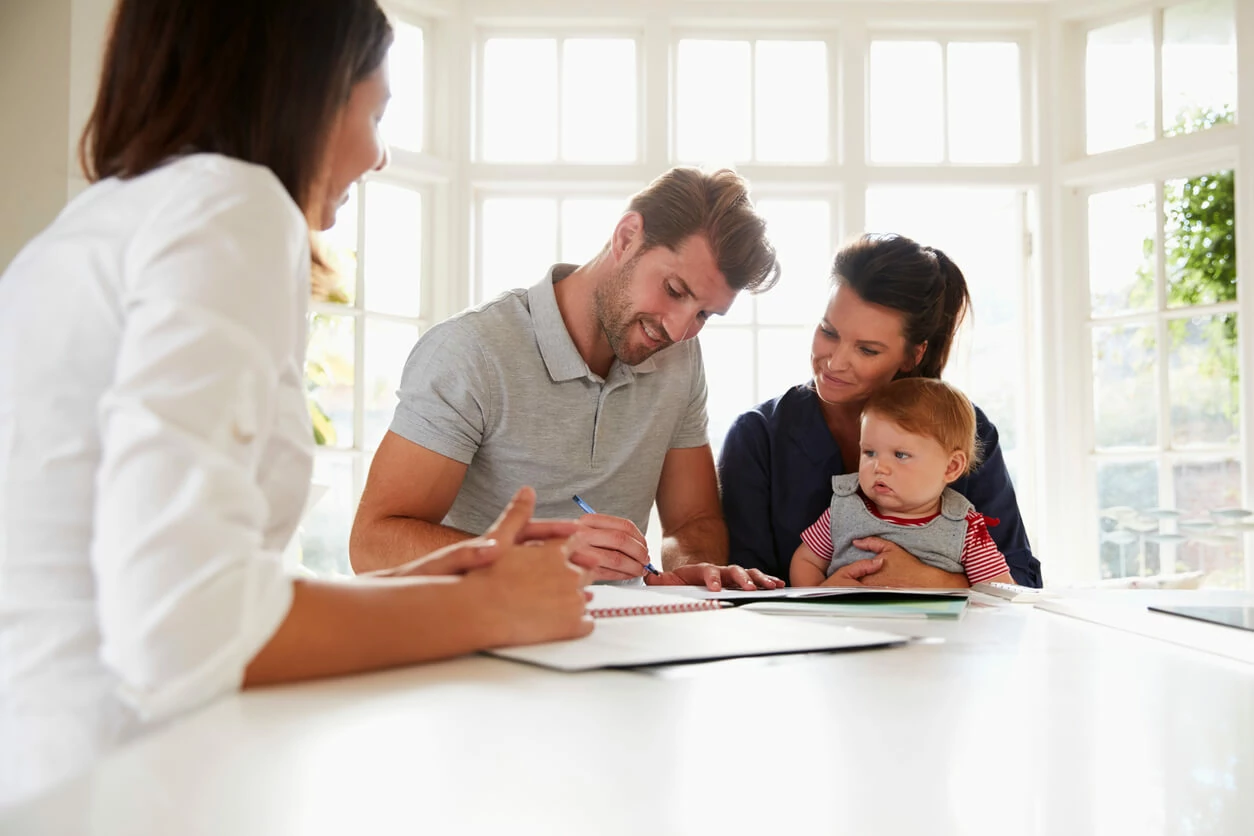 Père de famille signant un document à côté de sa famille et d'une professionnelle.