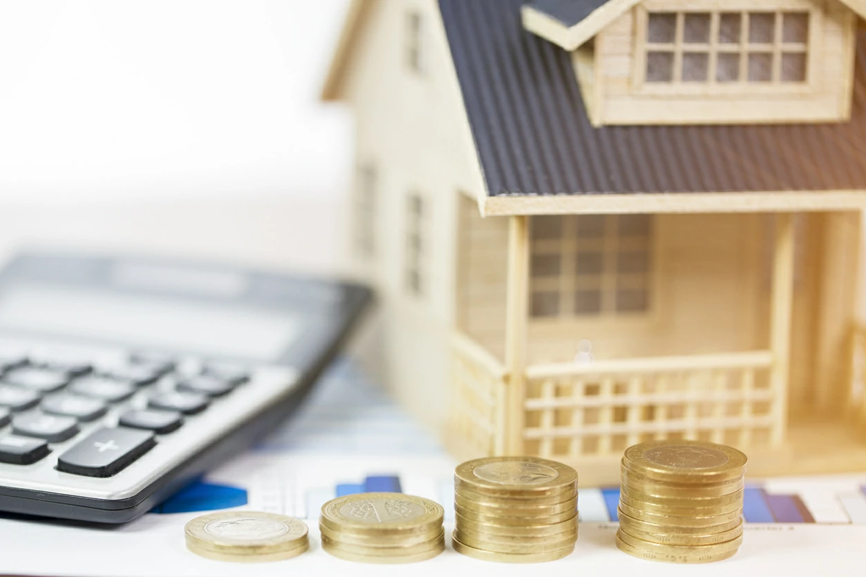 Quatre piles de pièces de monnaie, une calculatrice et une maisonnette.
