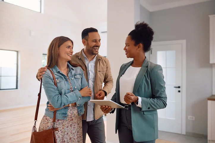 Un couple souriant devant une professionnel de l'immobilier qui tient une tablette.