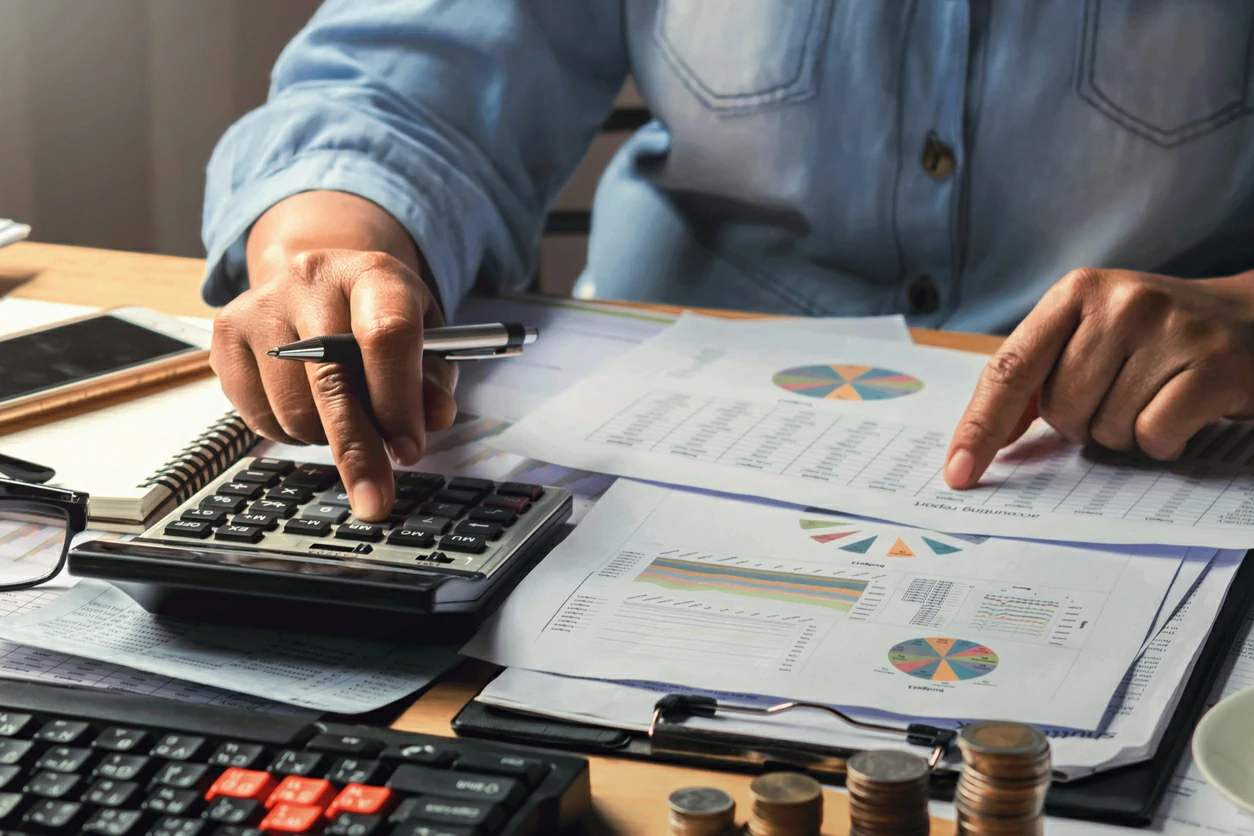Homme qui utilise une calculatrice en face de plusieurs documents financiers.