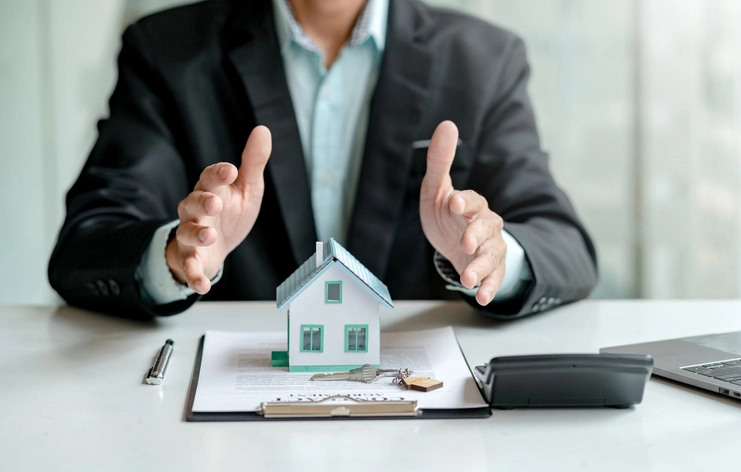 Homme qui tend les deux mains au-dessus d'une maison décorative posée sur un document.