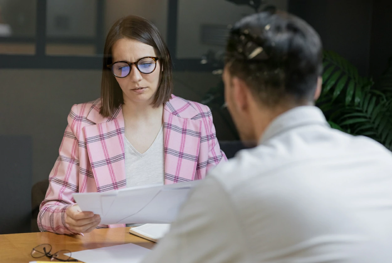 Femme à lunettes consultant des dossiers en face d'un homme.