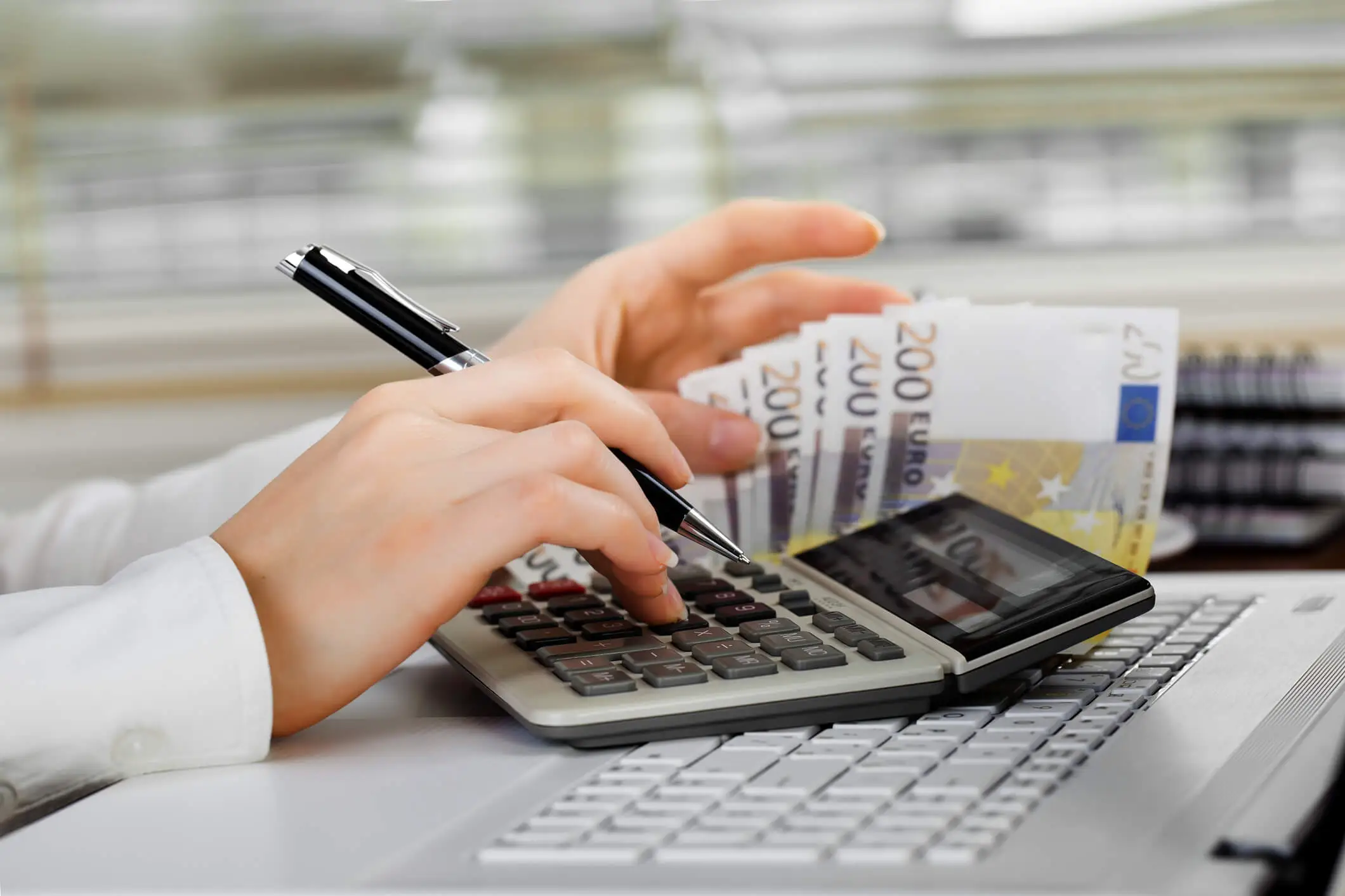 Femme comptant de l'argent avec une calculatrice au-dessus d'un ordinateur portable.