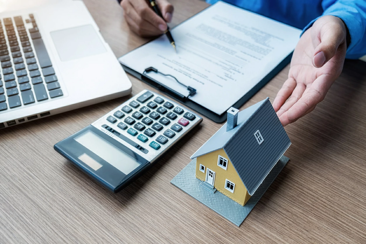 Homme consultant des documents à côté d'une maquette de maison, une calculatrice et un ordinateur portable 