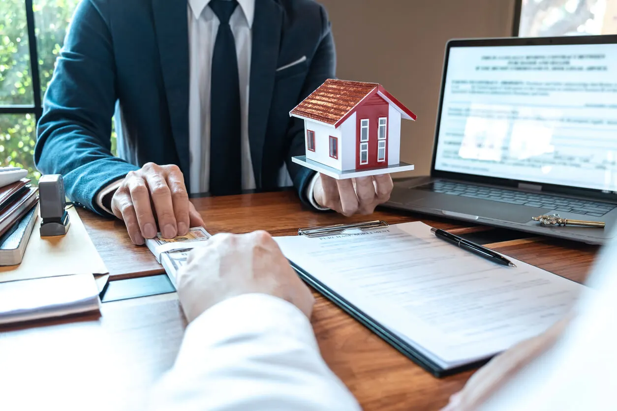 Homme tenant une maquette de maison en face d'un homme qui lui donne une liasse de billet.